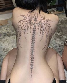 a woman is sitting on the floor with her back turned to show an intricate tattoo design