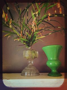 a green vase sitting on top of a table next to a green vase filled with flowers