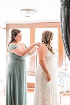 two women standing in front of a mirror and one is adjusting the bride's dress