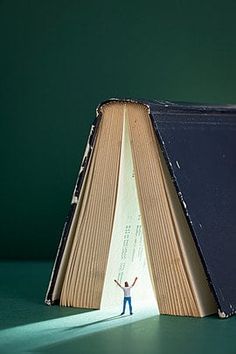 an open book with a person standing in front of it on a green table top