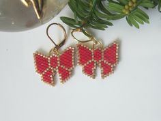 three red bow shaped beaded earrings sitting on top of a white table next to a plant