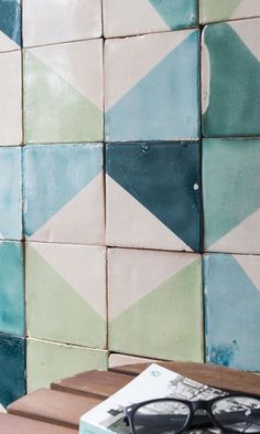 a pair of black glasses sitting on top of a wooden table next to a blue and green tiled wall