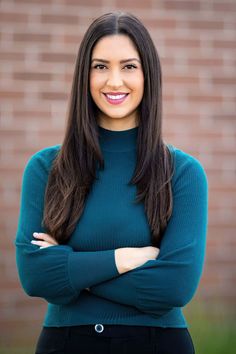 a smiling woman with her arms crossed in front of a brick wall and green sweater