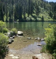 the water is crystal green and there are rocks on the ground in front of it