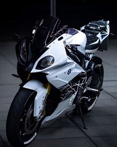 a white and black motorcycle parked on top of a cement floor next to a pole