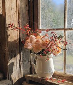 a white pitcher filled with flowers sitting on top of a window sill next to a window