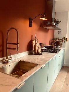 a kitchen with an orange wall and marble counter tops, copper faucets and brass fixtures