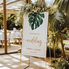 a sign that says welcome to your wedding with greenery and flowers on it in front of some tables