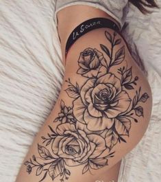 a woman laying on top of a bed with tattoos on her stomach and flowers in the thigh