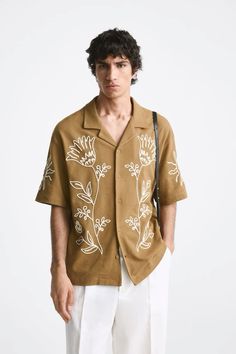 a young man wearing a brown shirt with white flowers on the front and back, standing in