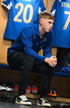 a man squatting on the floor in front of some blue shirts and shoes with numbers on them