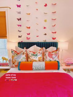 the bed has many colorful pillows on it and is next to a wall with butterflies