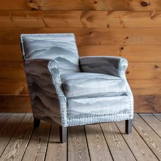 an upholstered chair sits on a wooden floor in front of a wood paneled wall