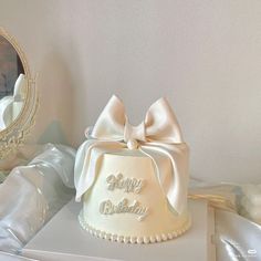 a white birthday cake with a bow on top and a mirror behind it in a room