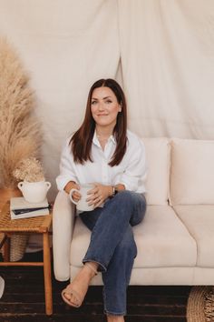 a woman sitting on top of a white couch next to a table and potted plant