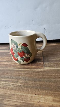 a coffee cup with strawberries on it sitting on a wooden table next to a wall