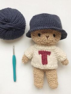 a crocheted teddy bear next to a ball of yarn and a knitting needle