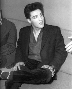 a black and white photo of a man in a suit sitting on the floor with his hands crossed