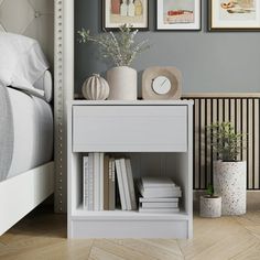 a white nightstand with books and vases on it in front of a gray wall