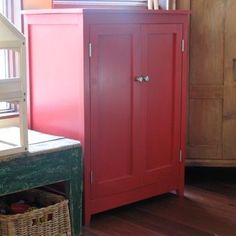 a red cabinet sitting on top of a hard wood floor next to a wooden dresser