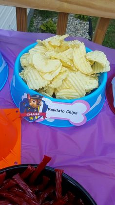 some chips are sitting in bowls on a purple tablecloth with an orange plate next to it