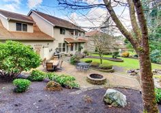 an outdoor patio and landscaping area in front of a house with trees, rocks, and bushes