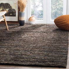 a living room area with a rug, chair and vases on the floor in front of a window