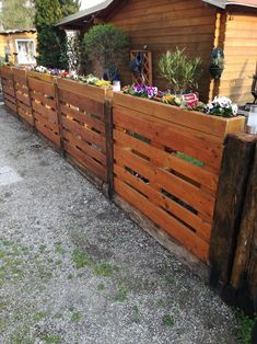 a wooden fence with plants growing on top and in the middle, next to a building