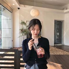 a woman standing on a porch holding a drink in her hand and looking down at the ground