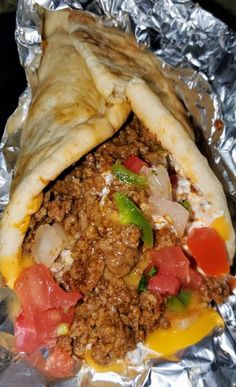 a burrito with meat, cheese and tomatoes on top of tin foil wrapped in aluminum foil