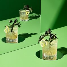 two glasses filled with lemonade and garnishes on a green table top