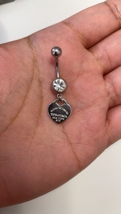 a person is holding a tiny belly ring with a heart charm on it's side