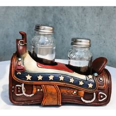 two mason jars are sitting on top of a cowboy's saddle with the stars and stripes painted on it