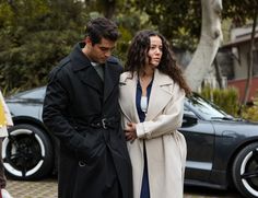 a man and woman standing next to each other in front of a black sports car