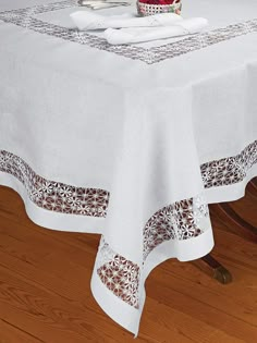 a white table cloth with brown and white designs on the border is sitting on a wooden floor