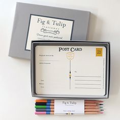 a set of four colored pencils sitting in a box next to a postcard