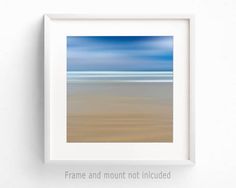 a white frame hanging on the wall above a beach with blue sky and ocean in the background