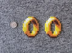 two pieces of perler bead sitting on top of a gray surface next to a penny