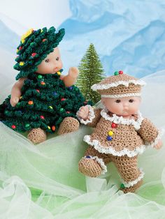 two small crocheted dolls sitting next to each other in front of a christmas tree