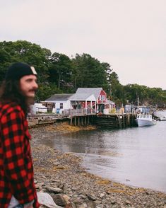 a man with long hair standing on the shore looking at boats docked in the water