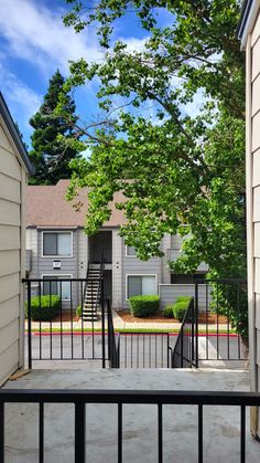 an apartment complex with trees and stairs leading to the front door, through which is a fence