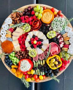 a platter filled with lots of different types of cheeses and fruits on top of a table