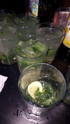 several glasses filled with water and lemons on top of a black table next to bottles