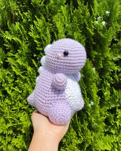 a hand holding a small crocheted stuffed animal in front of some green bushes