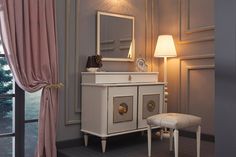 a white dresser sitting in front of a window next to a lamp and a chair