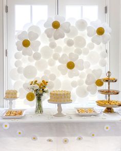 a white table topped with lots of cake and desserts next to a large balloon wall