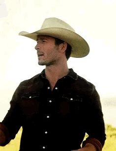 a man wearing a cowboy hat and holding a wine glass in his hand while standing in a field