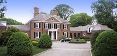 a large red brick house surrounded by trees and bushes with cars parked in front of it