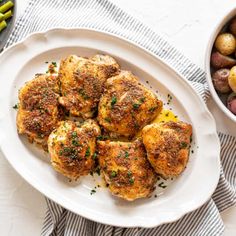 a white plate topped with chicken and potatoes next to a bowl of green beans on a table