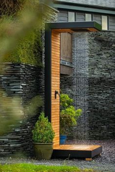 an outdoor shower is shown in front of a house with stone walls and green grass